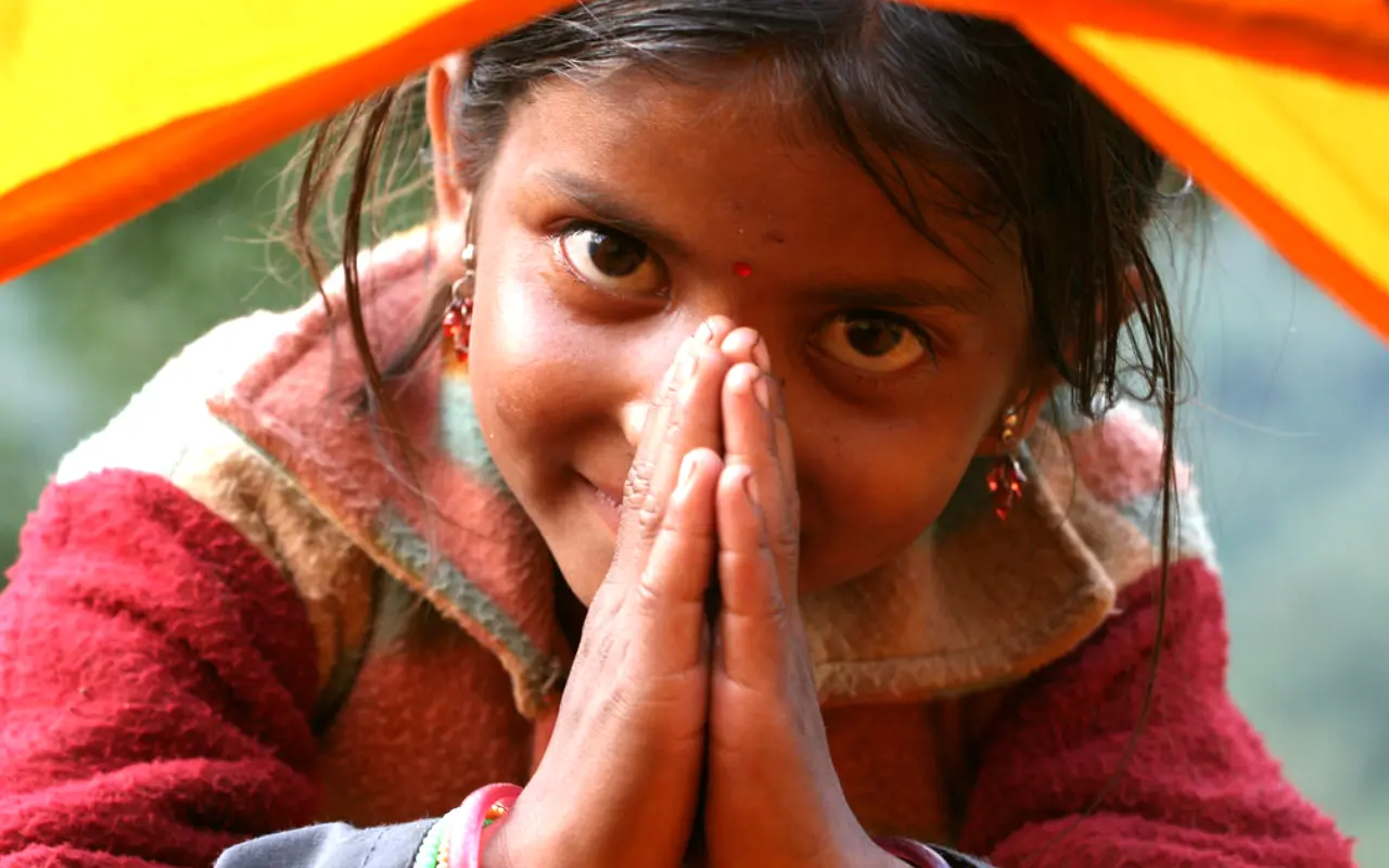 A little girl warmly greets with folded hands, saying Namaste